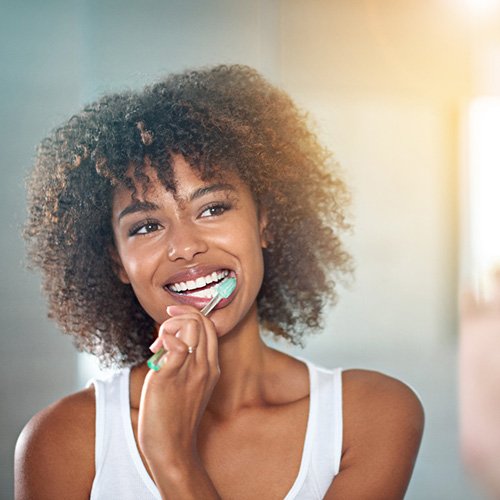 Woman brushing her beautiful teeth at bathroom mirror