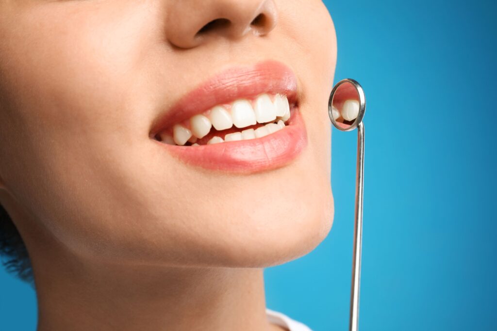 Nose-to-neck 3/4 profile of woman smiling with dental mirror reflecting teeth