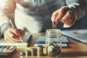 Person calculating budget and putting coins in a jar. 
